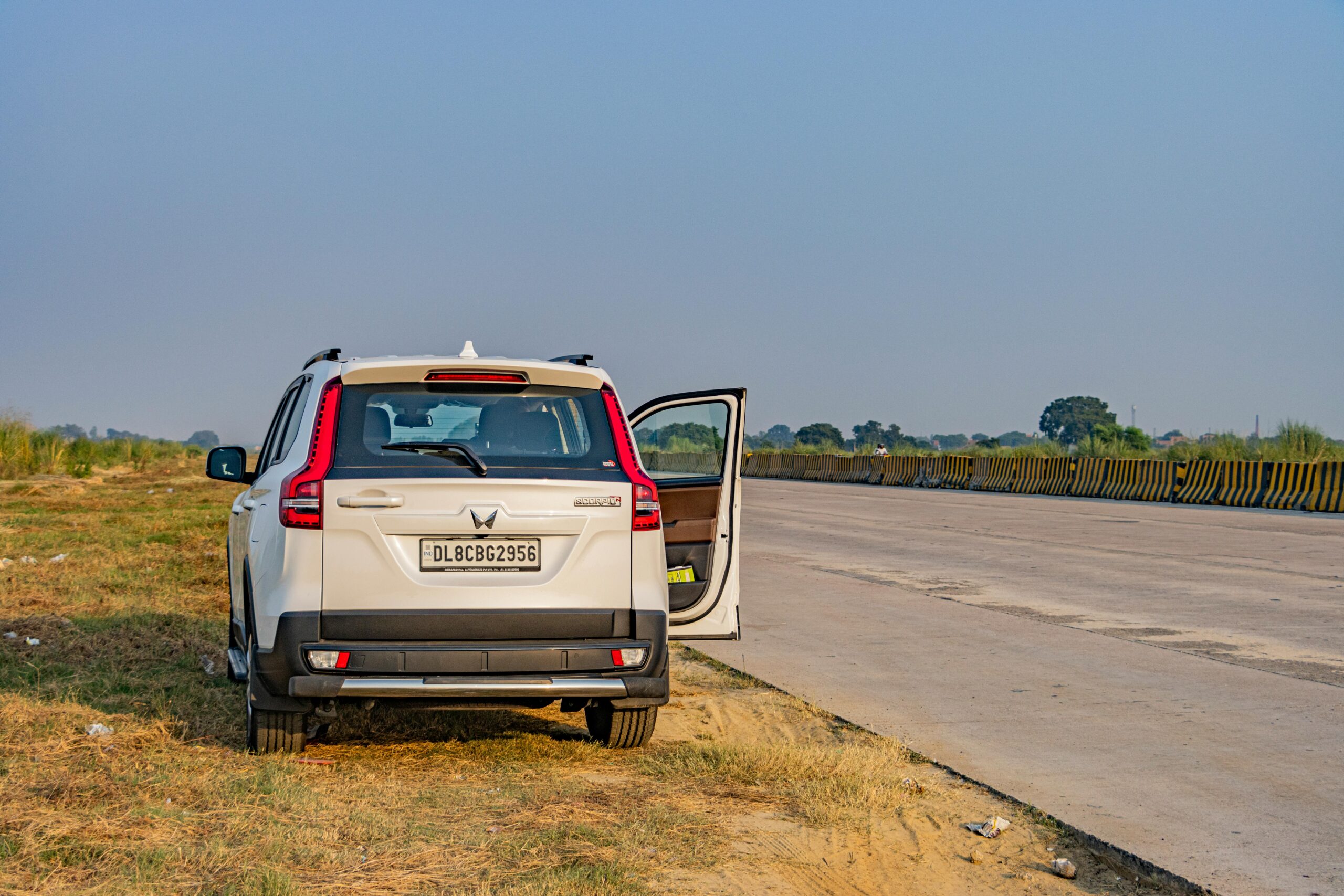 A white SUV parked on a deserted Indian highway during daytime, capturing the vast open road and landscape.